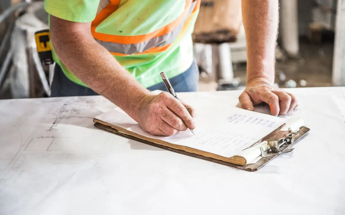 Hands writing on a clipboard at a job site table